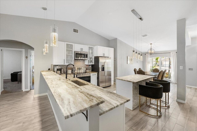 kitchen with a breakfast bar area, hanging light fixtures, glass insert cabinets, appliances with stainless steel finishes, and a peninsula