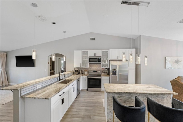 kitchen featuring appliances with stainless steel finishes, glass insert cabinets, a peninsula, pendant lighting, and a sink