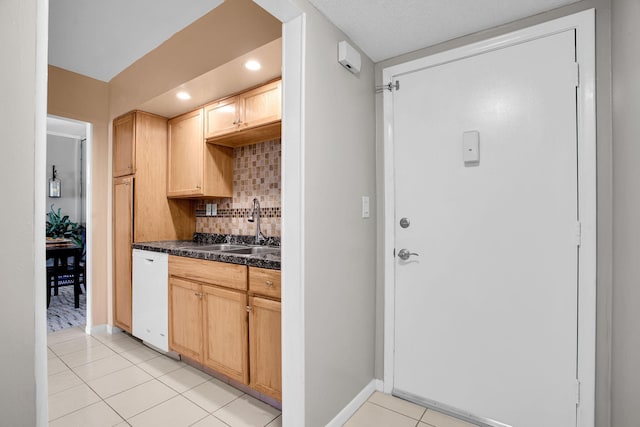 kitchen with white dishwasher, light tile patterned flooring, a sink, tasteful backsplash, and dark countertops