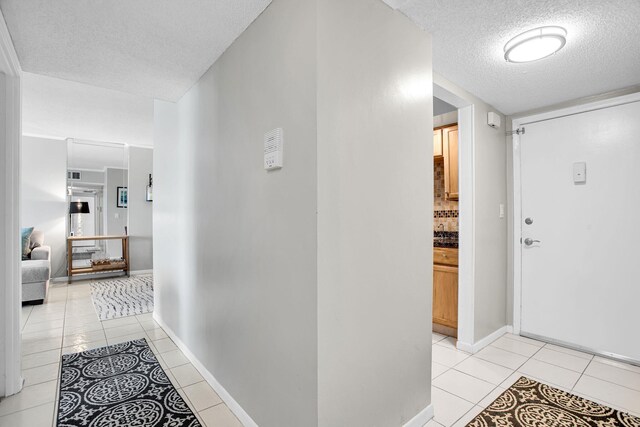 corridor featuring a textured ceiling, light tile patterned flooring, and baseboards