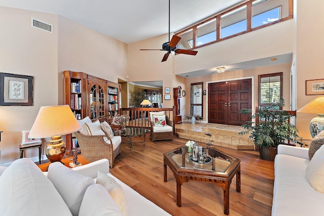 living area with a ceiling fan, a high ceiling, visible vents, and wood finished floors