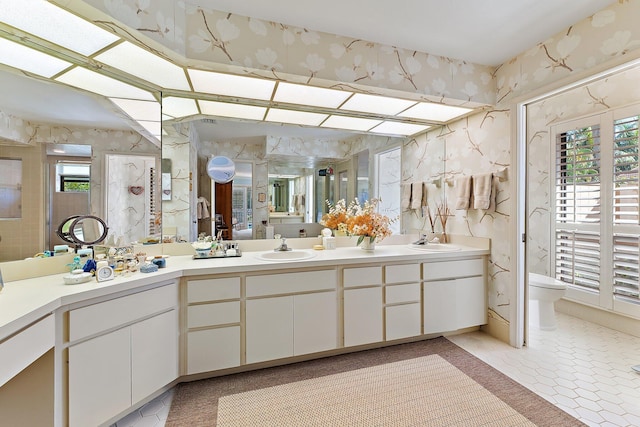 full bathroom featuring double vanity, a sink, toilet, and wallpapered walls