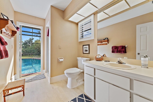 bathroom featuring wallpapered walls, baseboards, toilet, wood finished floors, and vanity