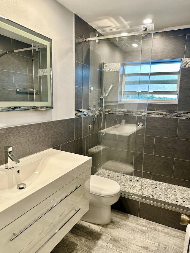 bathroom with tile walls, toilet, a stall shower, vanity, and wood finished floors