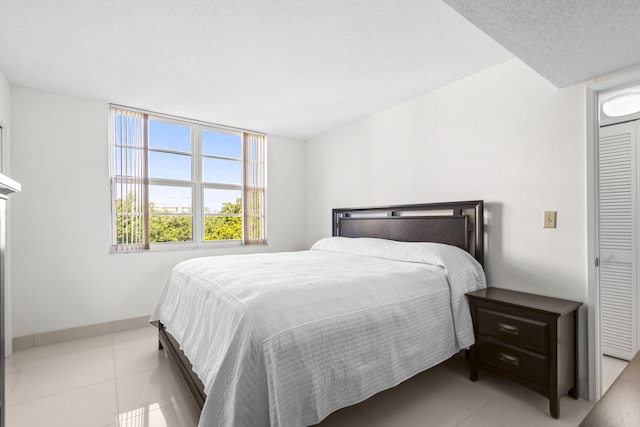 bedroom with baseboards, a textured ceiling, and light tile patterned flooring