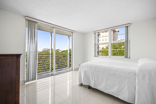 bedroom featuring access to exterior, floor to ceiling windows, a textured ceiling, and light tile patterned floors