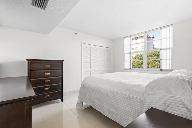 bedroom featuring light tile patterned floors, a textured ceiling, visible vents, and a closet