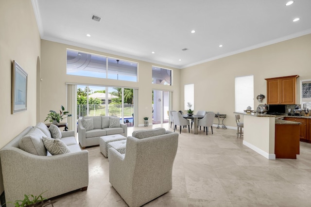 living area with baseboards, a high ceiling, visible vents, and ornamental molding