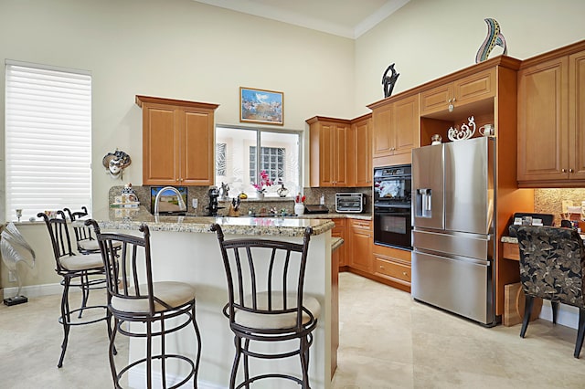 kitchen with light stone counters, decorative backsplash, brown cabinetry, a peninsula, and stainless steel fridge with ice dispenser