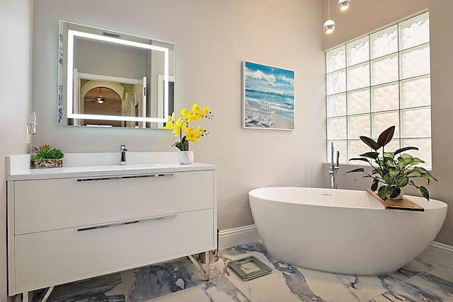 bathroom with marble finish floor, a soaking tub, vanity, and baseboards