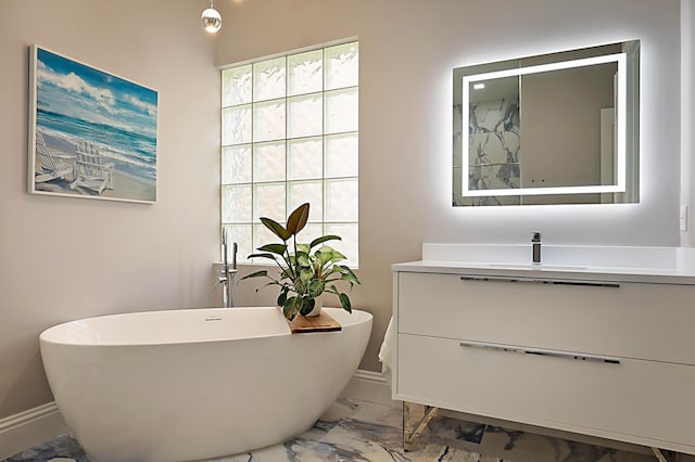 bathroom featuring marble finish floor, baseboards, a freestanding tub, and vanity