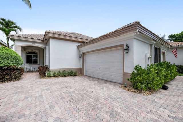 view of front facade featuring decorative driveway, an attached garage, a tile roof, and stucco siding