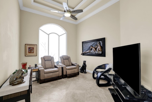 living area featuring a tray ceiling, ornamental molding, a ceiling fan, and baseboards