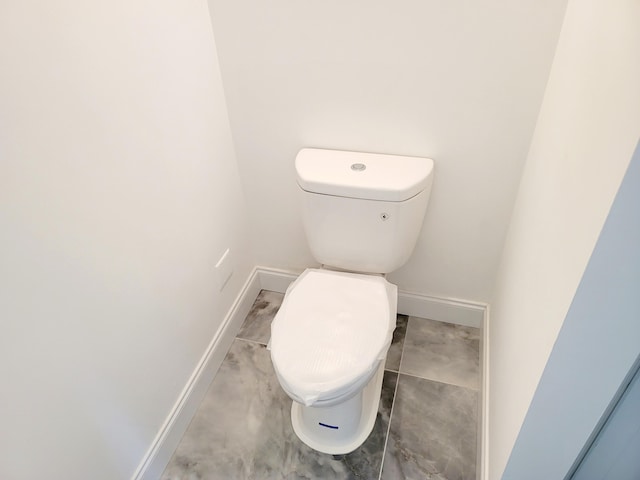 bathroom featuring baseboards, concrete floors, and toilet