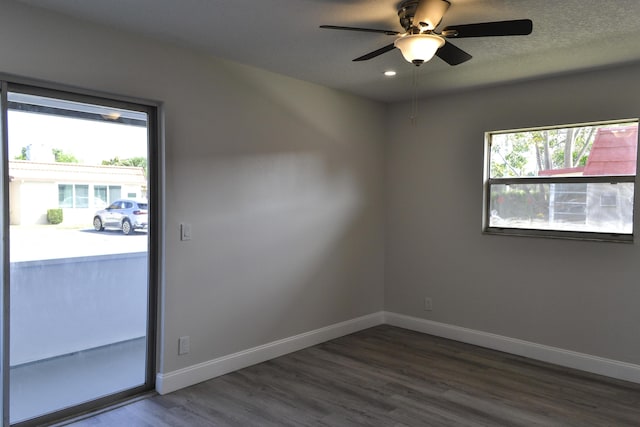 unfurnished room featuring dark wood-style floors, a wealth of natural light, a textured ceiling, and baseboards