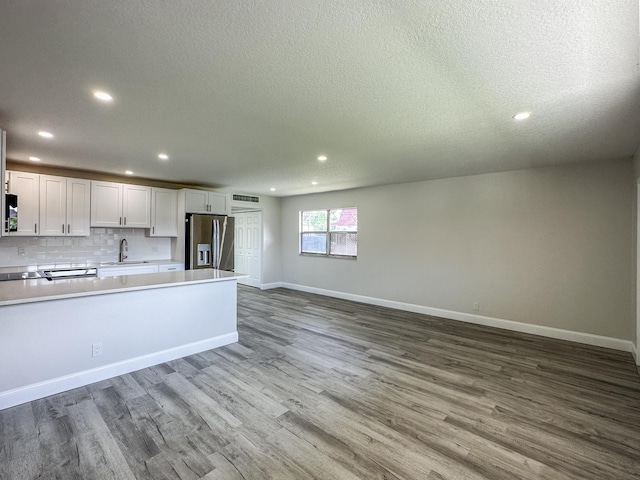 kitchen featuring stainless steel refrigerator with ice dispenser, white cabinetry, a sink, wood finished floors, and a peninsula