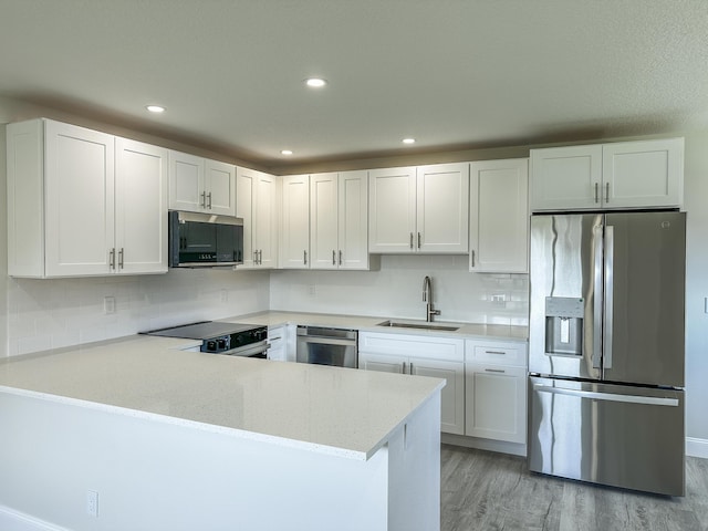 kitchen with stainless steel appliances, a peninsula, a sink, decorative backsplash, and light wood finished floors