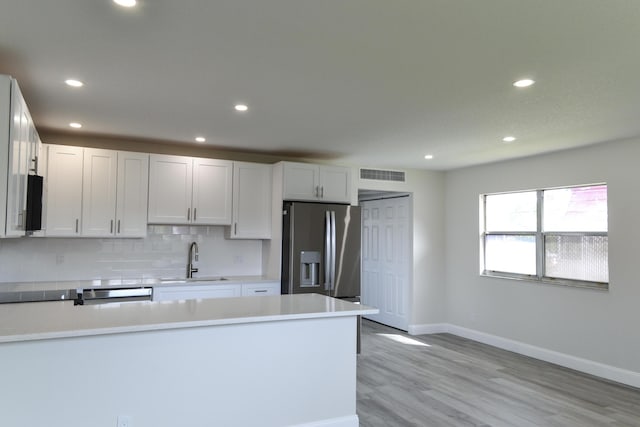 kitchen featuring visible vents, decorative backsplash, light countertops, stainless steel refrigerator with ice dispenser, and a sink