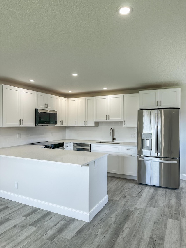 kitchen with light wood-style flooring, stainless steel appliances, light countertops, white cabinetry, and a sink