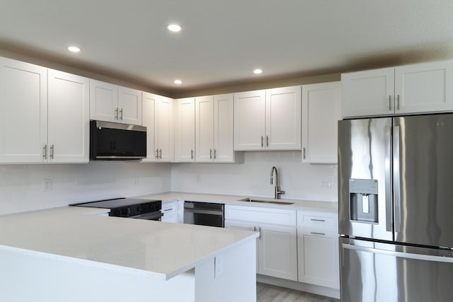 kitchen with tasteful backsplash, appliances with stainless steel finishes, a peninsula, white cabinetry, and a sink