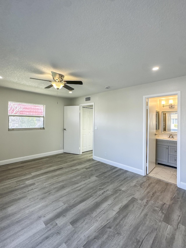 unfurnished bedroom with visible vents, baseboards, wood finished floors, a textured ceiling, and a sink