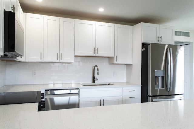 kitchen with stainless steel appliances, a sink, visible vents, white cabinets, and decorative backsplash