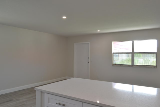 kitchen with baseboards, light stone countertops, light wood-style floors, white cabinetry, and recessed lighting