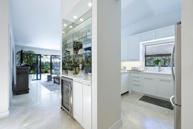 kitchen featuring beverage cooler, a sink, white cabinetry, backsplash, and freestanding refrigerator