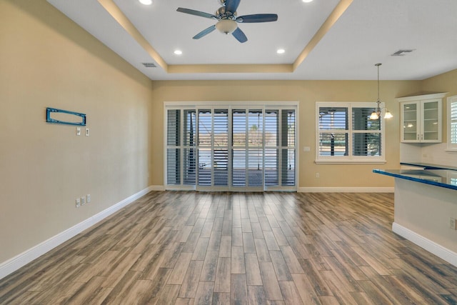 unfurnished living room with recessed lighting, wood finished floors, visible vents, baseboards, and a raised ceiling