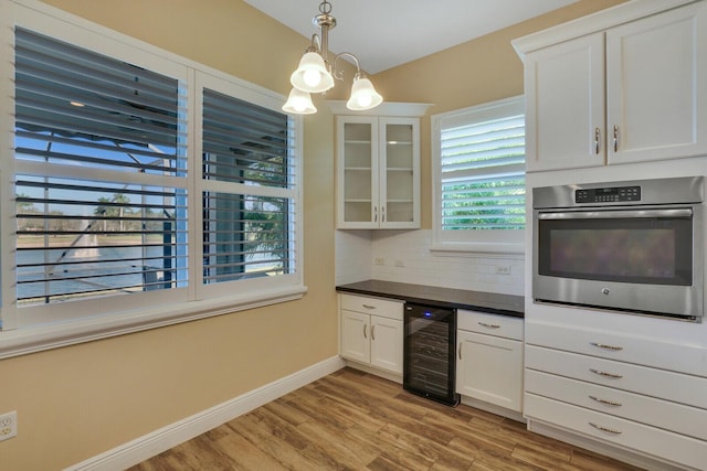 kitchen featuring beverage cooler, white cabinets, dark countertops, glass insert cabinets, and oven