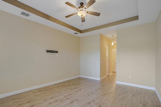 unfurnished room featuring ceiling fan, light wood-style flooring, baseboards, and a raised ceiling