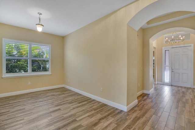 entryway with light wood-type flooring, baseboards, arched walkways, and a notable chandelier