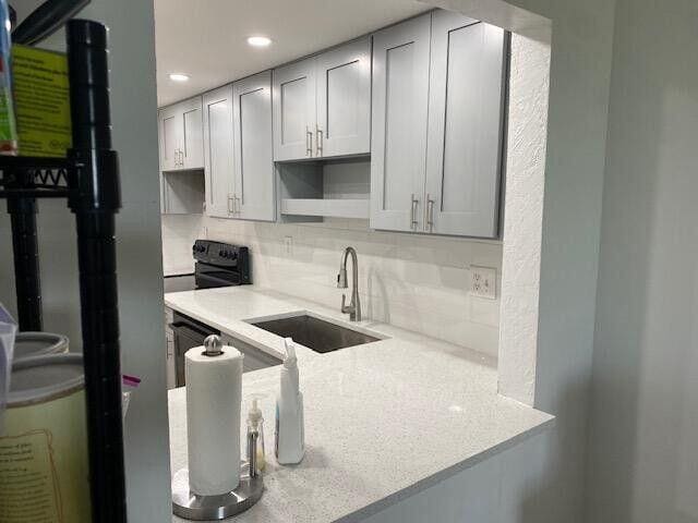 kitchen featuring backsplash, black electric range oven, light countertops, and a sink