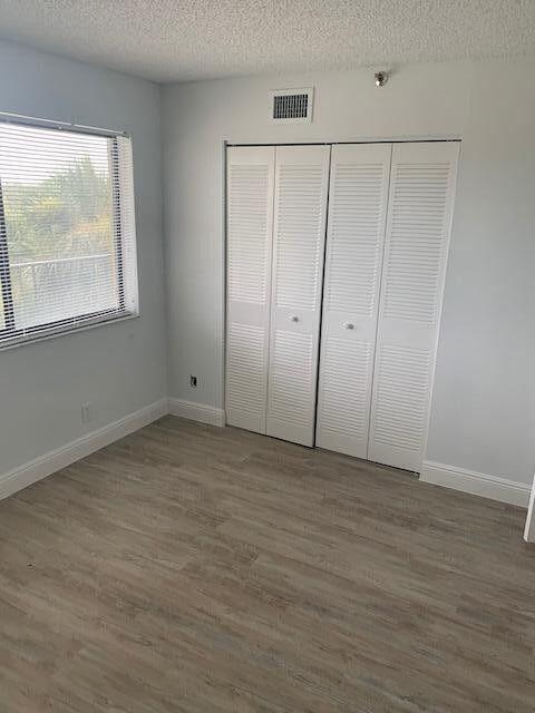 unfurnished bedroom featuring a closet, visible vents, dark wood-type flooring, a textured ceiling, and baseboards