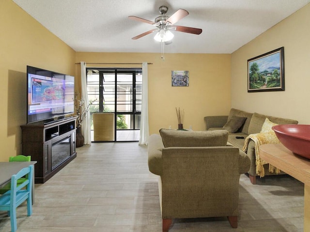 living room with light wood finished floors, ceiling fan, and a glass covered fireplace