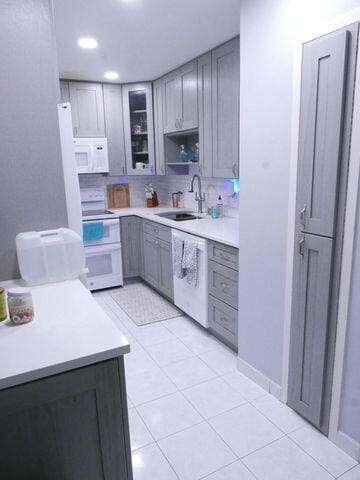 kitchen featuring gray cabinetry, white appliances, a sink, light countertops, and glass insert cabinets