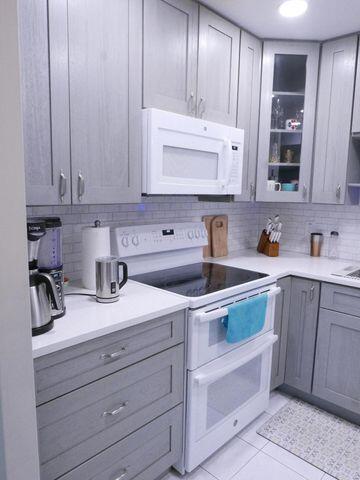 kitchen featuring light countertops, white appliances, gray cabinets, and glass insert cabinets