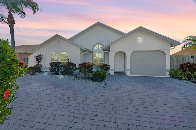 view of front of property with decorative driveway, an attached garage, and stucco siding