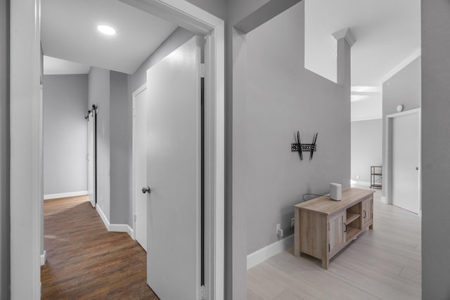 hallway featuring a barn door, light wood-style flooring, and baseboards