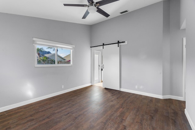 empty room with a barn door, baseboards, visible vents, a ceiling fan, and dark wood-type flooring