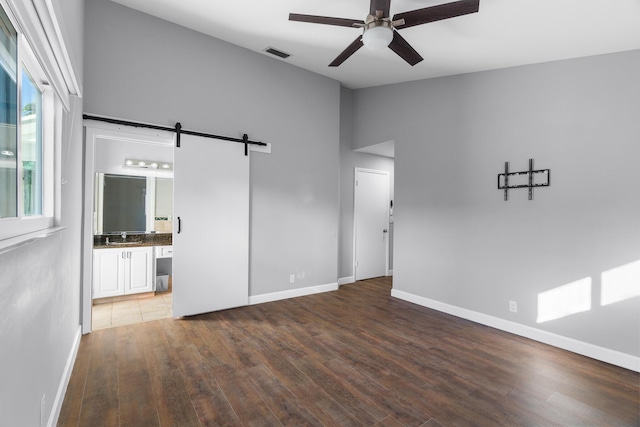 spare room with a barn door, visible vents, a ceiling fan, wood finished floors, and a sink