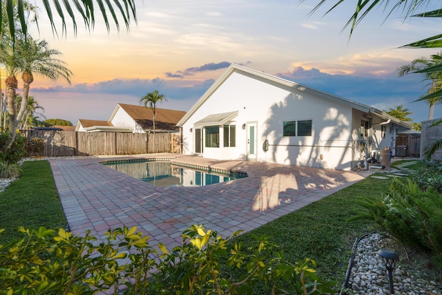 pool at dusk featuring a fenced in pool, a fenced backyard, a patio, and central AC