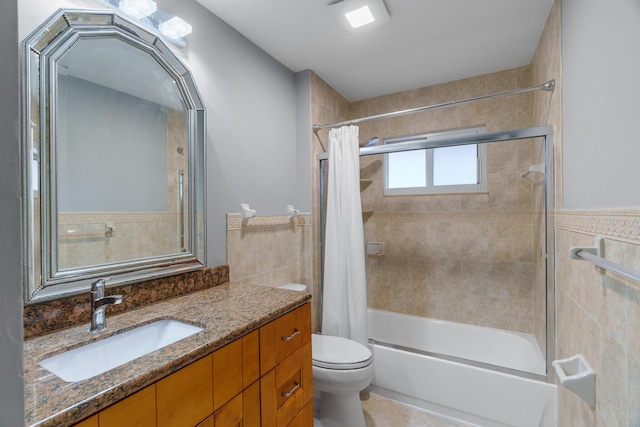 bathroom with toilet, a wainscoted wall, shower / bath combination with curtain, vanity, and tile walls