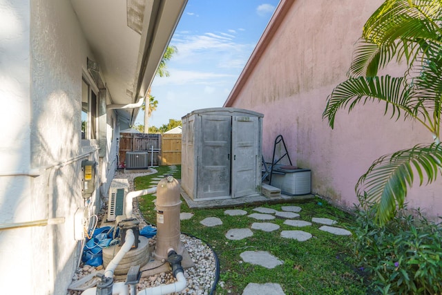 view of yard featuring an outbuilding, a storage unit, central AC unit, and fence