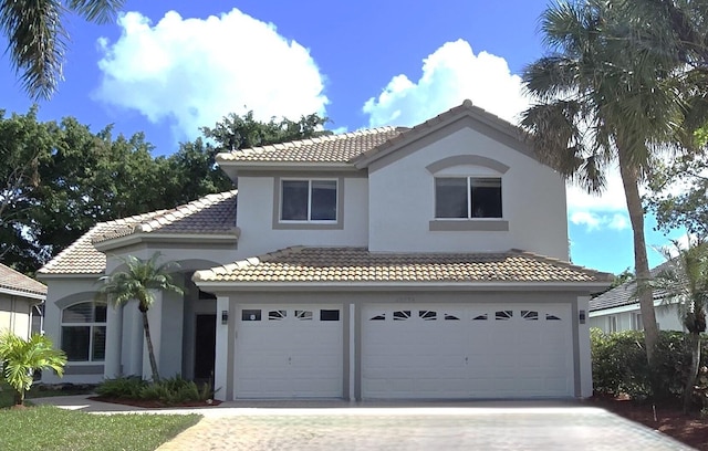 mediterranean / spanish house featuring a garage, a tile roof, decorative driveway, and stucco siding