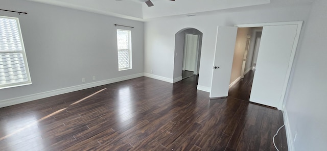 unfurnished room featuring arched walkways, dark wood-type flooring, a ceiling fan, and baseboards