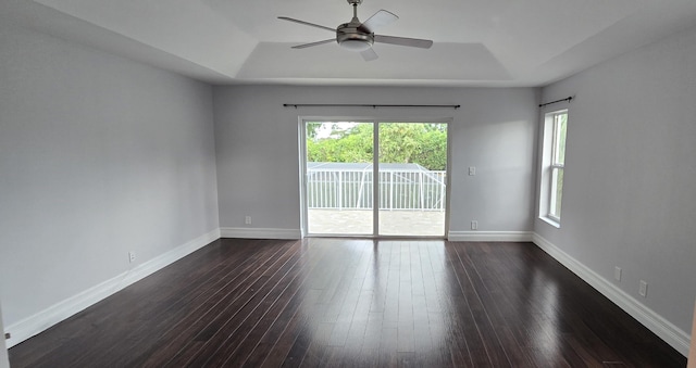 empty room featuring a raised ceiling, dark wood finished floors, and baseboards