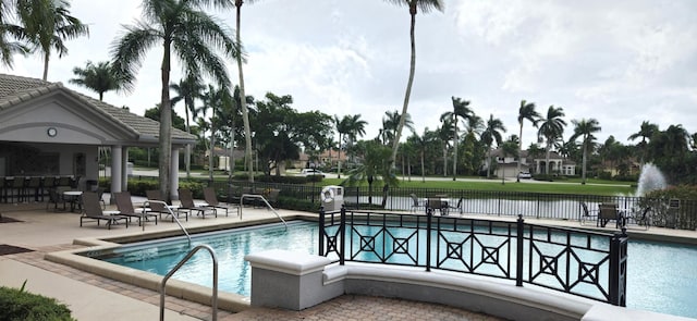 community pool with a patio, a water view, and fence