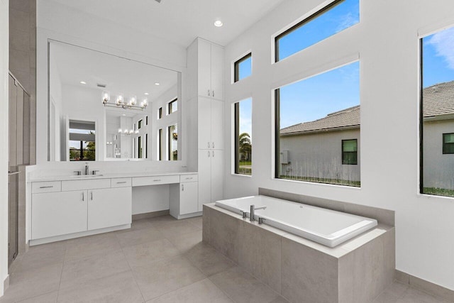 bathroom featuring an inviting chandelier, vanity, tile patterned flooring, baseboards, and a bath