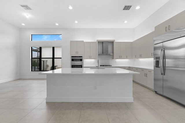 kitchen with visible vents, stainless steel appliances, wall chimney exhaust hood, and a center island with sink